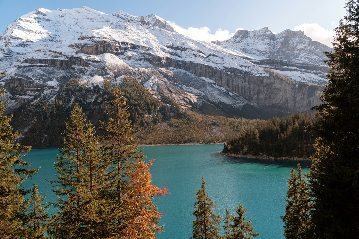 Turquoise lake with pine trees and snow-capped mountains.